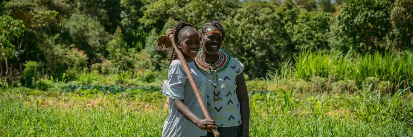 Woman and her daughter in their green field, standing together and smiling at the camera