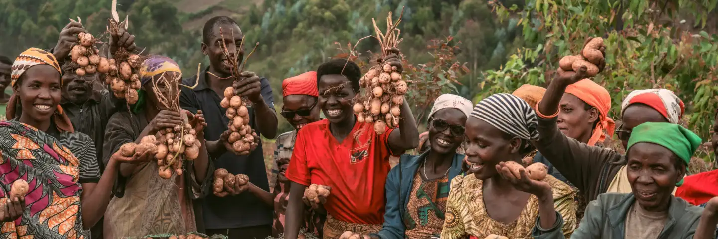 A group of farmers smiling and holding up freshly harvested potatoes in a field.