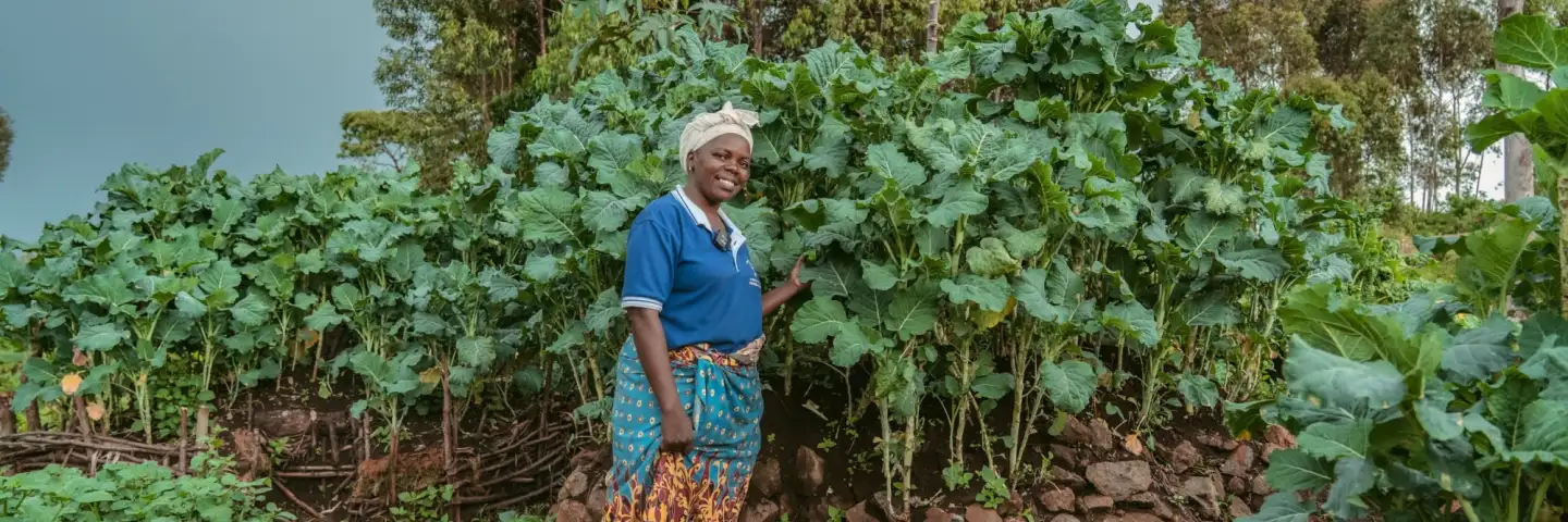 Carolyne, a Kenyan farmer, posing in front of her towering kitchen garden crops