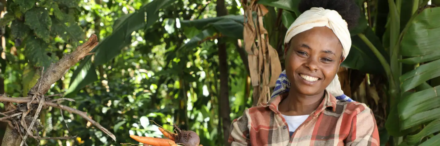 Ethiopian woman, smiling at the camera and holding carrots