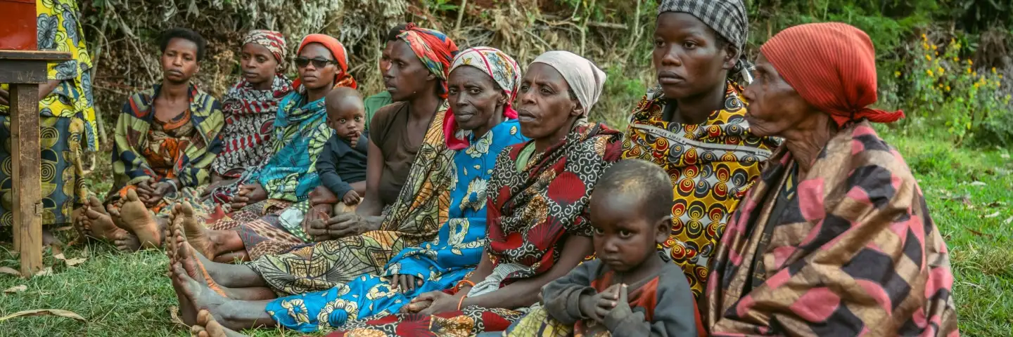 Burundian women sat next to each other, holding their children and wearing colourful outfits