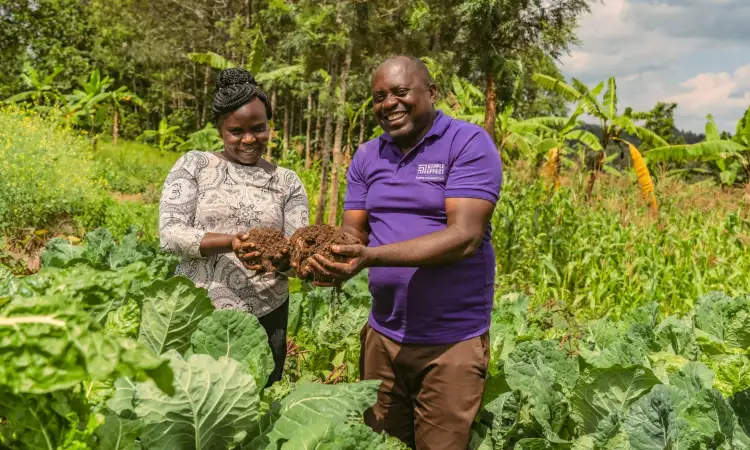 Kenyan farmer and Ripple Effect staff, standing in a lush green field holding soil