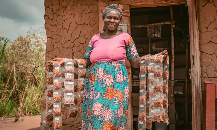 A Ugandan woman is outside her shop, posing with small bags of various confectionary items resting on both her arms