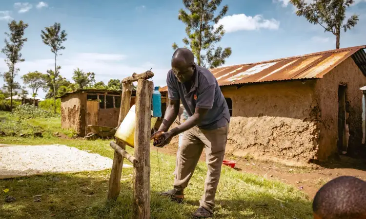 Daniel, project participant in Kenya, using a tip tap made of a plastic tub, hung on a wood frame and tilted with a string connected to a foot lever, to wash his hands