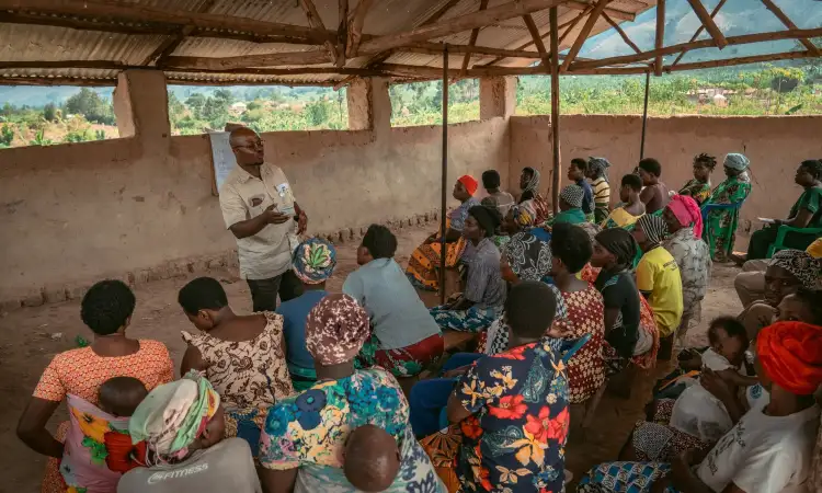 Ripple Effect field staff delivering a community training session in a refugee settlement, with dozens of people sat and listening