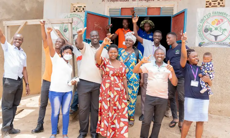 A dozen people standing in front of a building with their cooperative name on it, waving and smiling at the camera