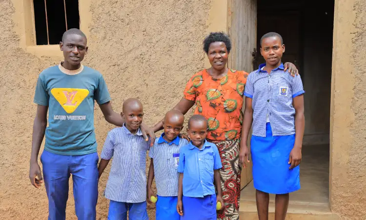Man, woman and four young children standing in front of their home, holding each other and smiling to the camera