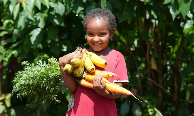 Young girl, daughter of previous Ripple Effect project participants, holding bananas and carrots her parents grew on their farm.