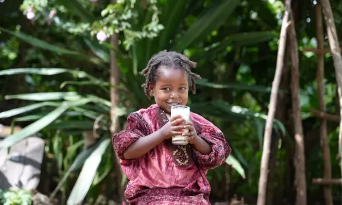 Little girl with a white moustache from her big cup of milk