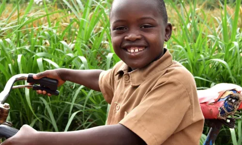 A young boy smiling while sitting on a bicycle in tall green grass