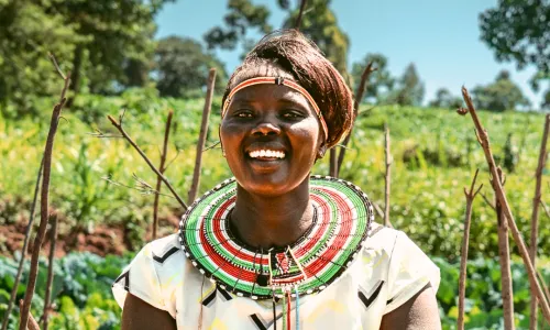 A woman smiling and holding a bowl of freshly harvested tomatoes in her vegetable garden.