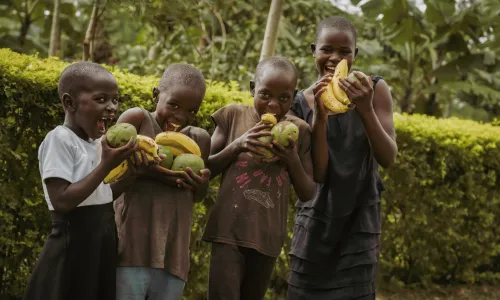 Four children smiling and laughing while holding bananas and mangoes from their family garden