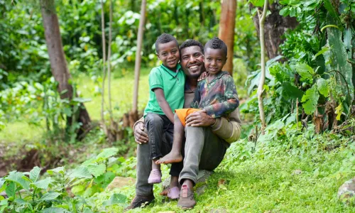 Father holding his two sons in a green field