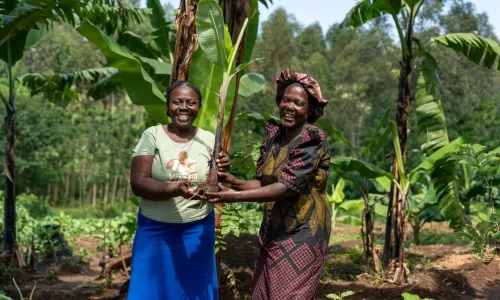 two women holding a banana sucker, smiling to the camera