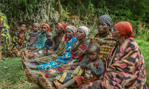 Burundian women sat next to each other, holding their children and wearing colourful outfits