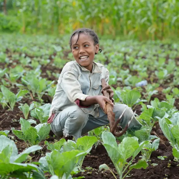 Young Ethiopian girl siting and smiling in a field of crops