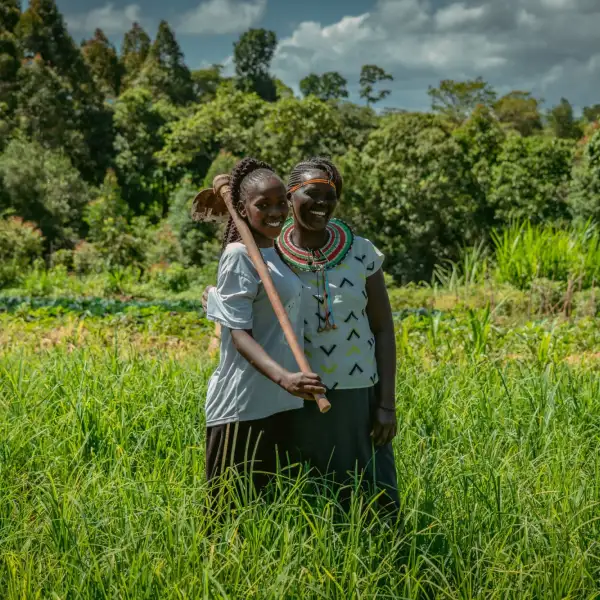 Two Kenyan women standing in a lush field, smiling