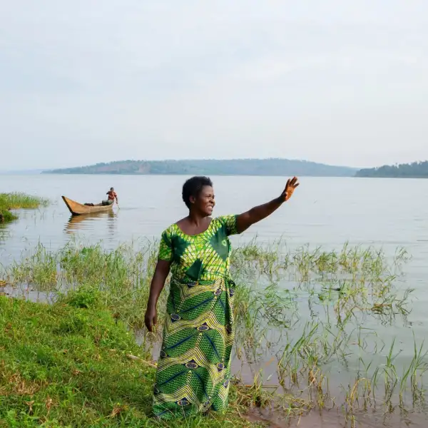 Jeanne, a Rwandan farmer, standing in front of a lake and waving at someone to the right