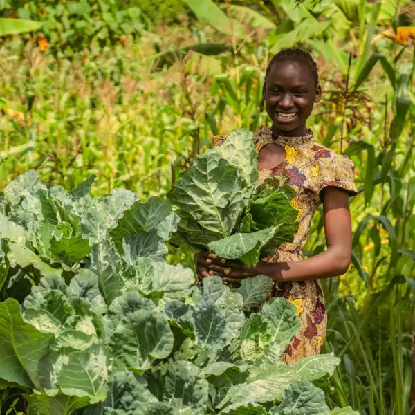 Young Kenyan woman showing her large cabbages she has grown, smiling